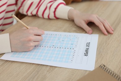 Photo of Student filling out answer sheet at wooden table indoors, closeup. Taking exam