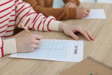 Photo of Students filling out answer sheet at wooden table indoors, closeup. Taking exam