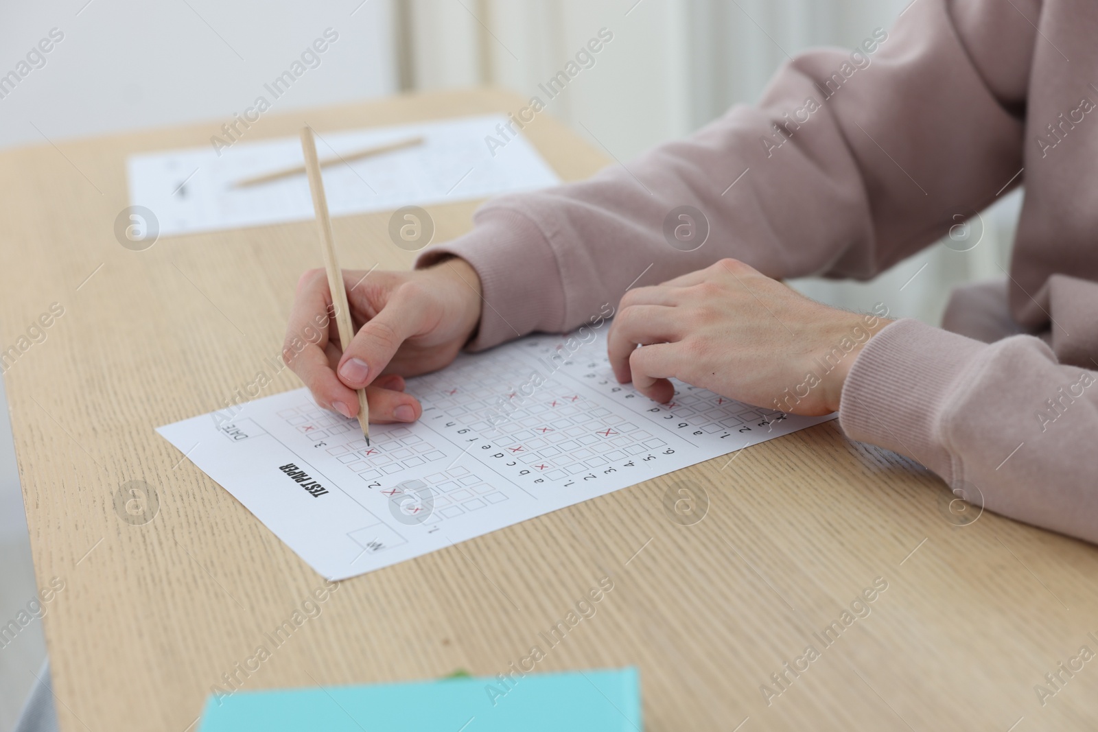Photo of Student filling out answer sheet at wooden table indoors, closeup. Taking exam
