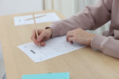Photo of Student filling out answer sheet at wooden table indoors, closeup. Taking exam