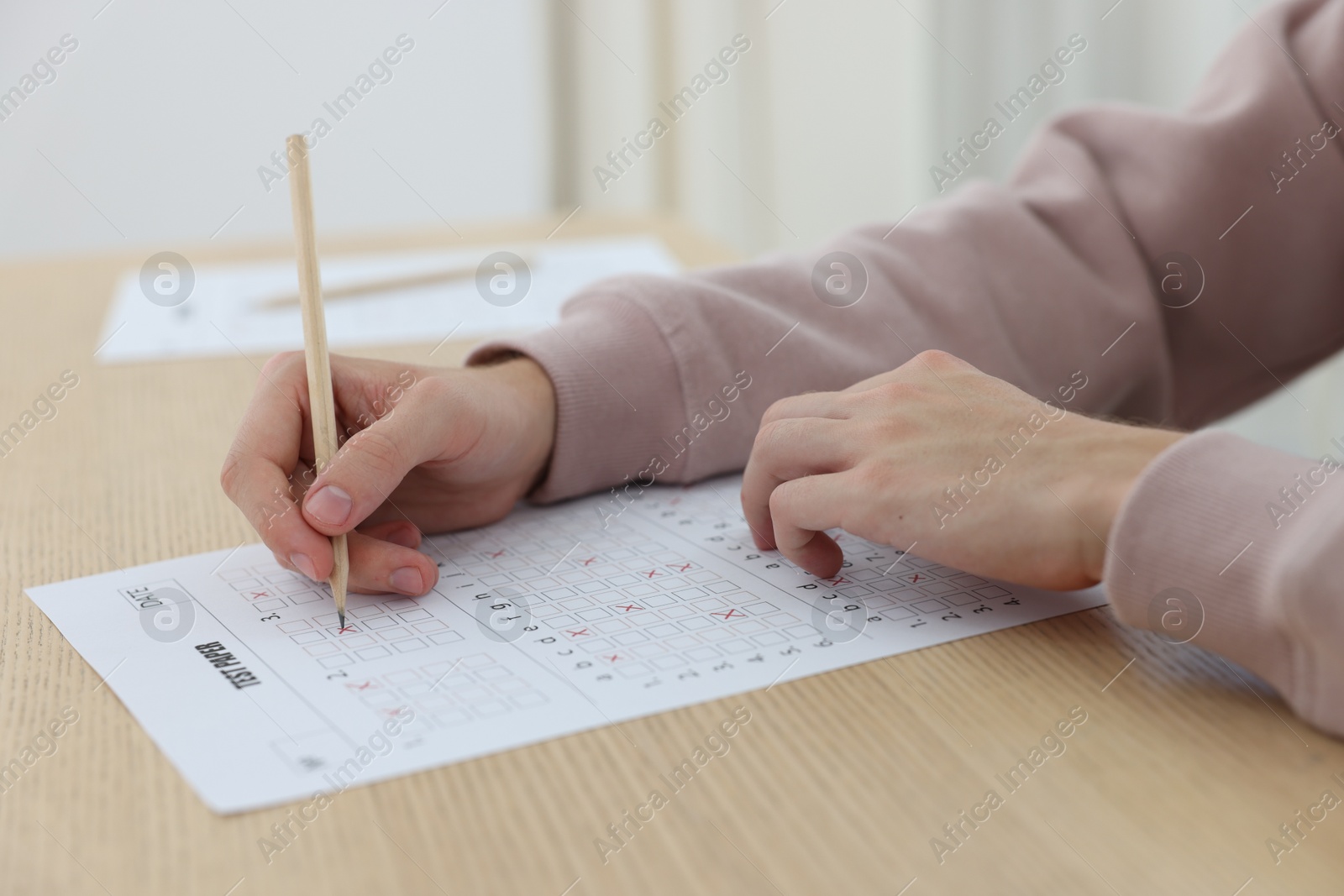 Photo of Student filling out answer sheet at wooden table indoors, closeup. Taking exam