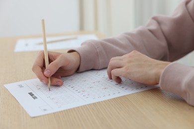Photo of Student filling out answer sheet at wooden table indoors, closeup. Taking exam