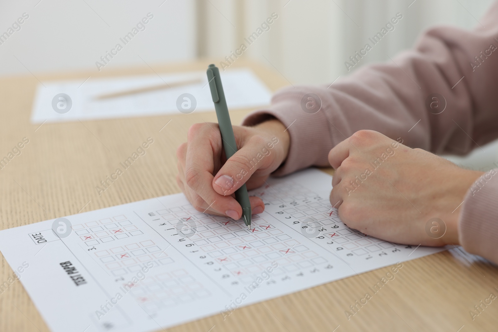 Photo of Student filling out answer sheet at wooden table indoors, closeup. Taking exam