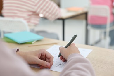 Photo of Student filling out answer sheet at wooden table indoors, closeup. Taking exam
