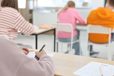 Photo of Students taking exam at wooden table indoors, selective focus