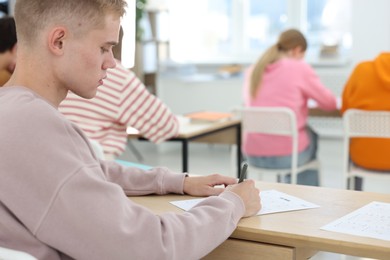 Photo of Students taking exam at wooden table indoors, selective focus