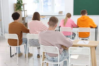 Photo of Students taking exam at wooden table indoors, back view