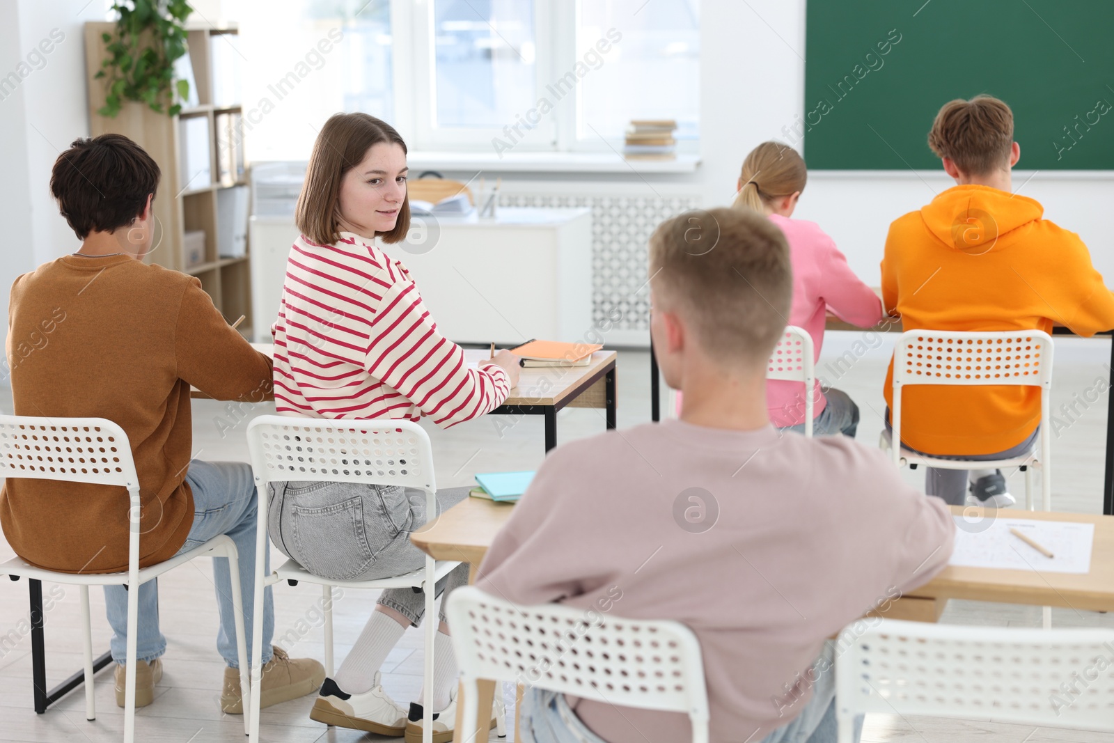 Photo of Students taking exam at wooden table indoors, back view