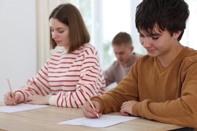 Photo of Students taking exam at wooden table indoors, selective focus