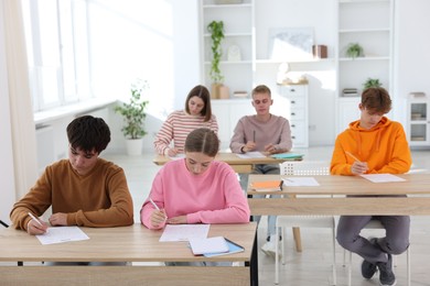 Photo of Students taking exam at wooden table indoors