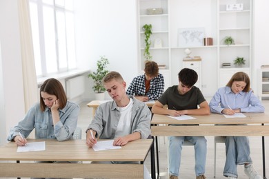 Photo of Students taking exam at wooden table indoors