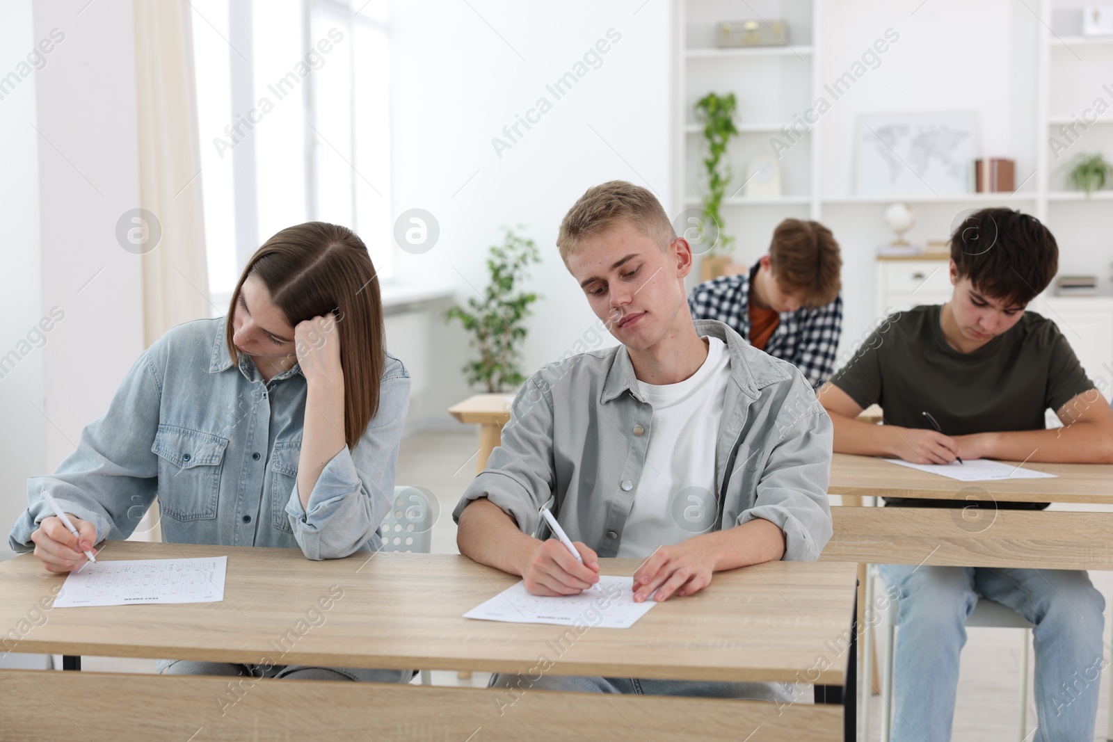 Photo of Students taking exam at wooden table indoors