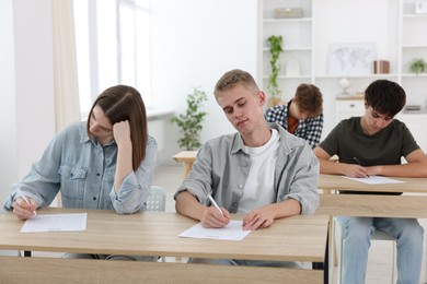 Photo of Students taking exam at wooden table indoors