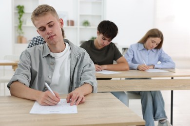 Photo of Students taking exam at wooden table indoors, selective focus