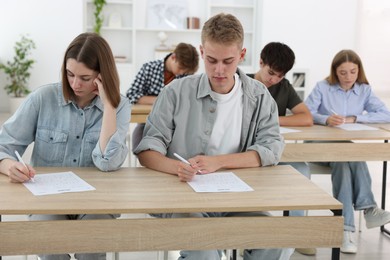 Photo of Students taking exam at wooden table indoors