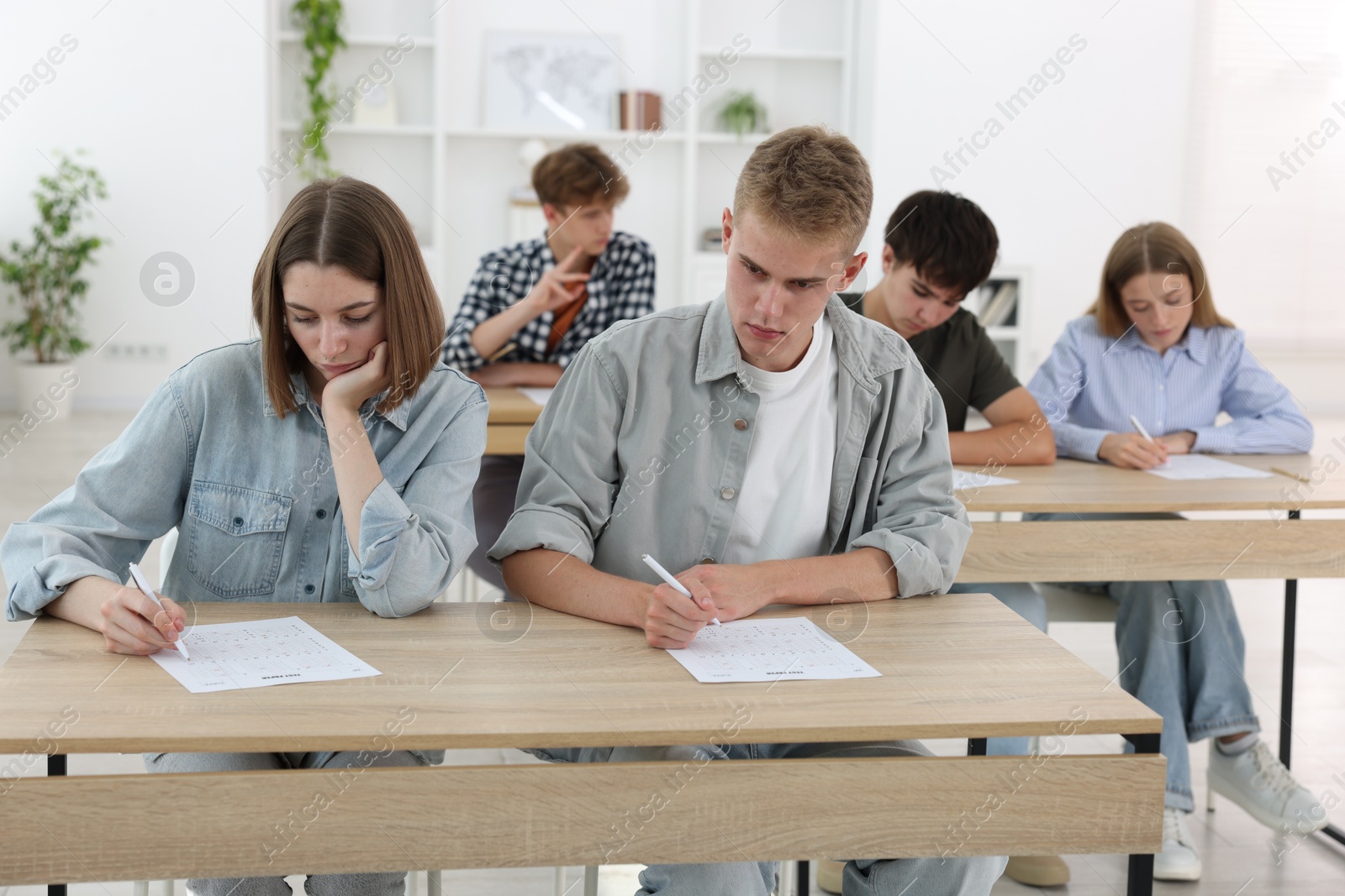 Photo of Students taking exam at wooden table indoors
