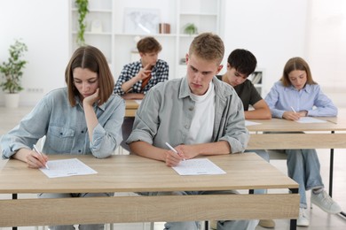 Photo of Students taking exam at wooden table indoors