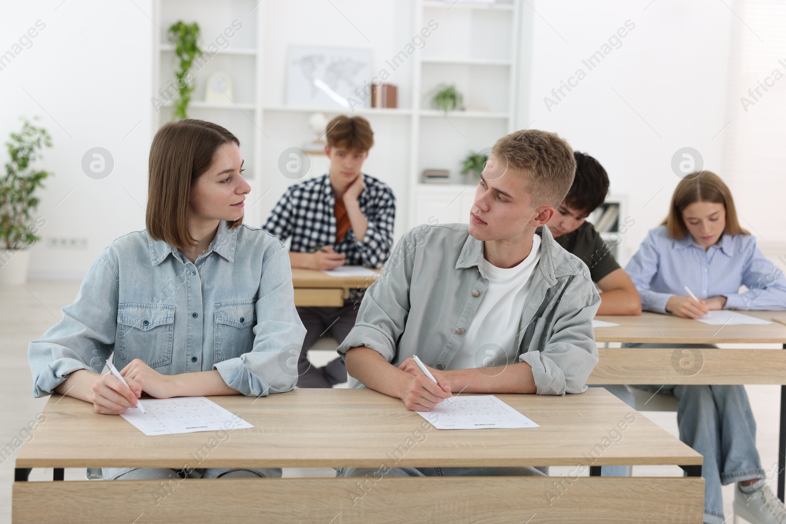 Photo of Students taking exam at wooden table indoors