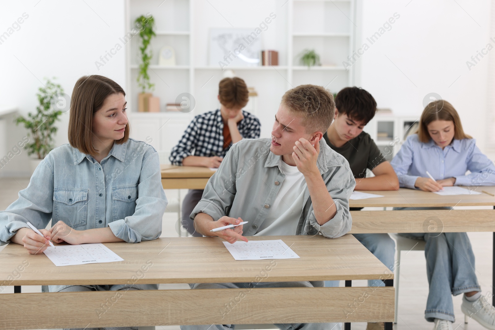 Photo of Students taking exam at wooden table indoors