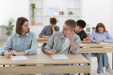 Photo of Students taking exam at wooden table indoors