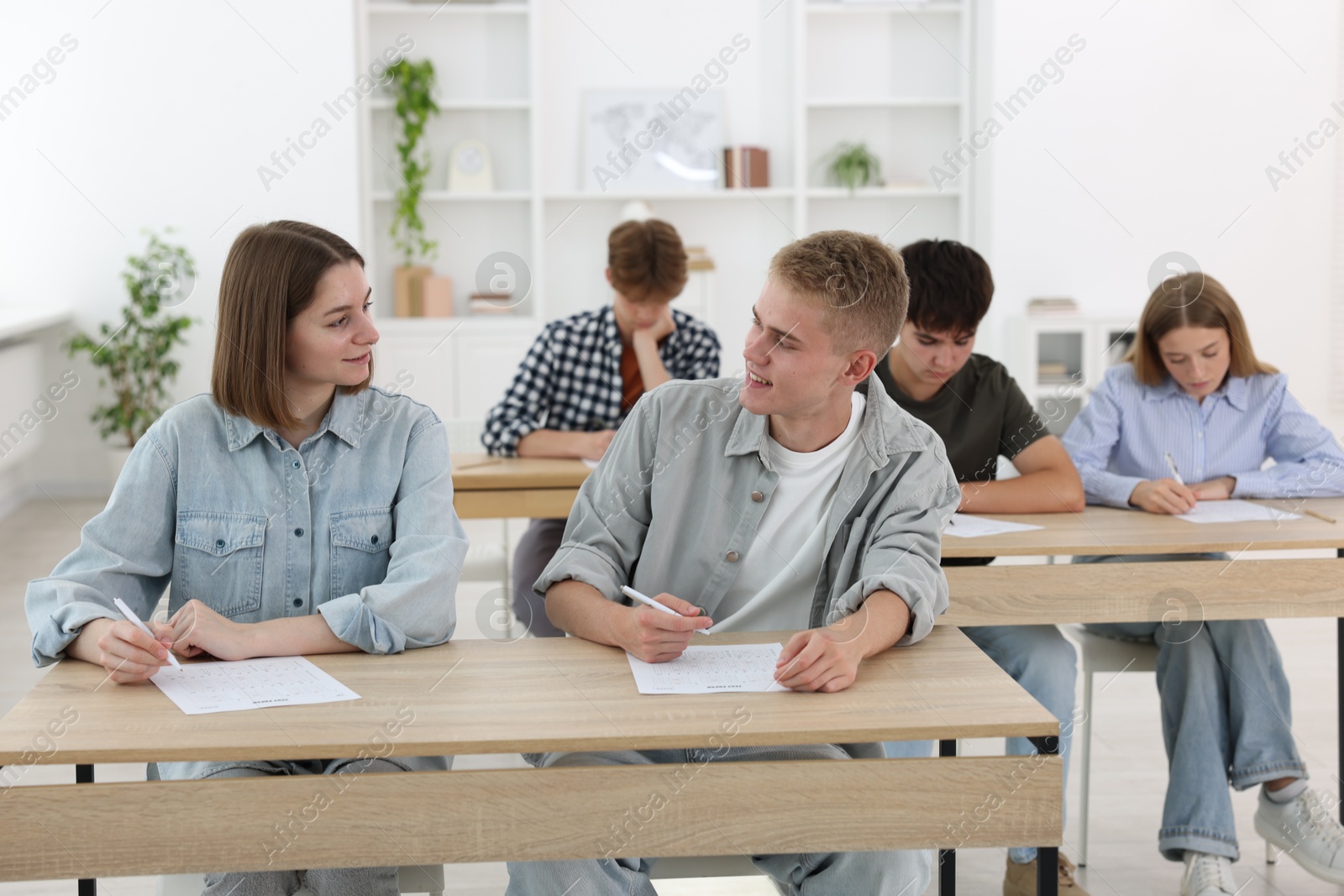 Photo of Students taking exam at wooden table indoors