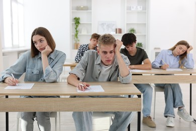 Photo of Students taking exam at wooden table indoors