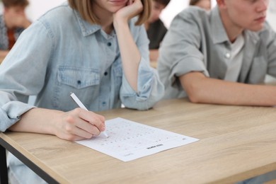 Photo of Students filling out answer sheet at wooden table indoors, closeup. Taking exam