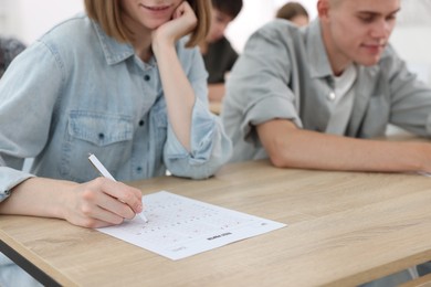 Photo of Students filling out answer sheet at wooden table indoors, selective focus. Taking exam