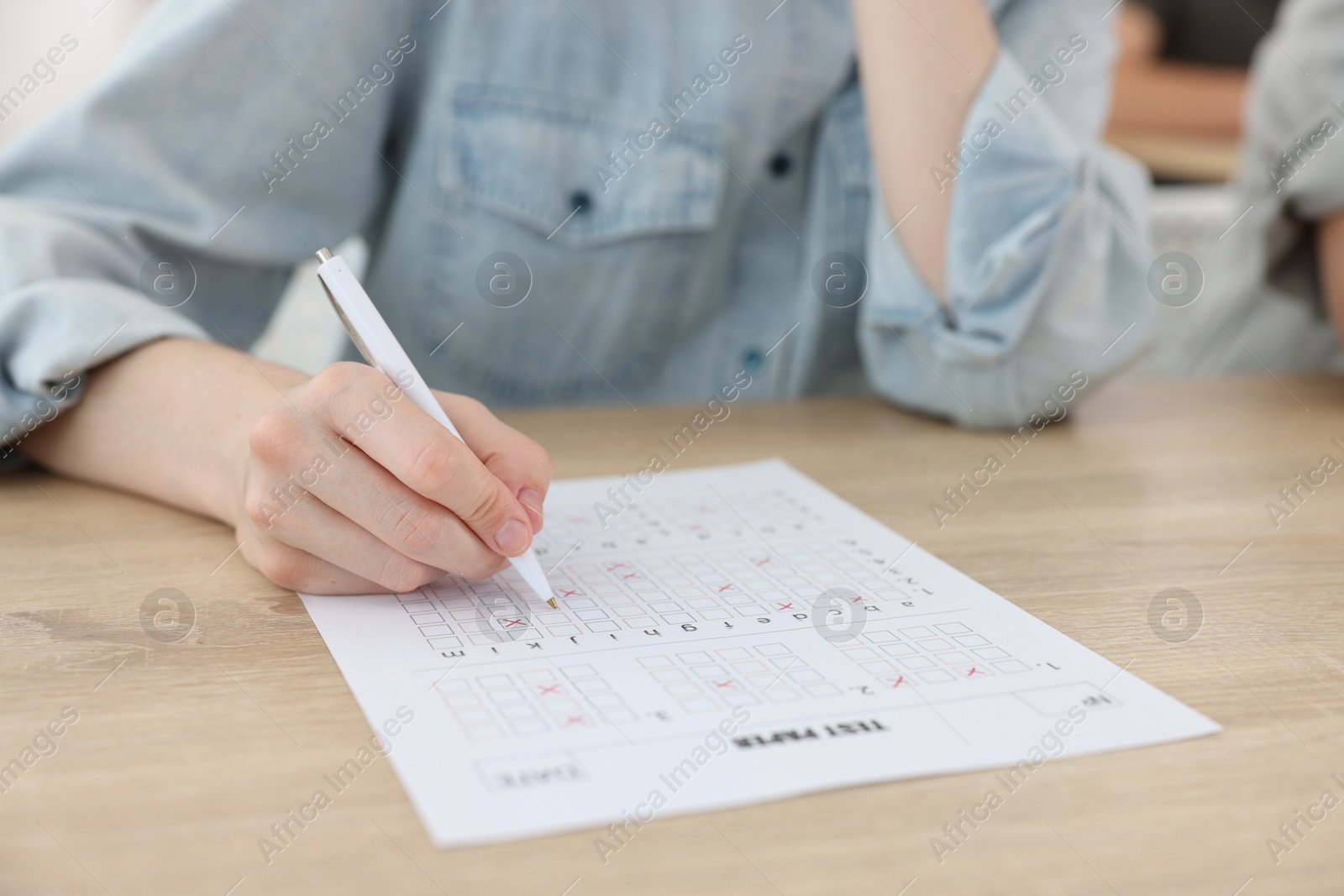 Photo of Student filling out answer sheet at wooden table indoors, closeup. Taking exam