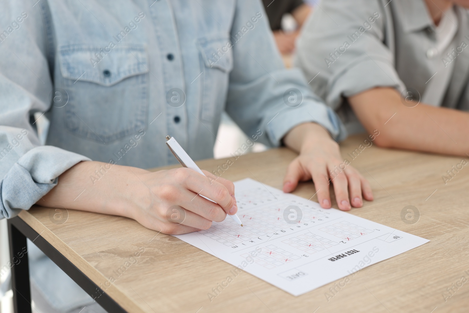 Photo of Students filling out answer sheet at wooden table indoors, closeup. Taking exam