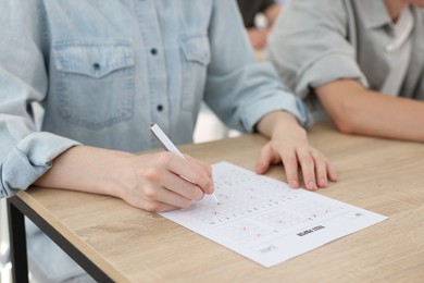 Photo of Students filling out answer sheet at wooden table indoors, closeup. Taking exam