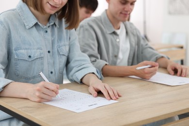 Photo of Students filling out answer sheet at wooden table indoors, selective focus. Taking exam