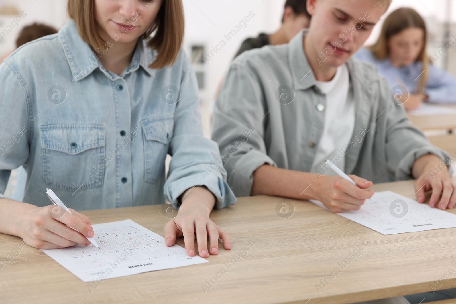 Photo of Students filling out answer sheet at wooden table indoors, selective focus. Taking exam