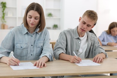 Photo of Students taking exam at wooden table indoors