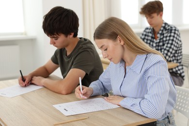 Photo of Students taking exam at wooden table indoors