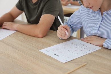 Photo of Students filling out answer sheet at wooden table indoors, closeup. Taking exam