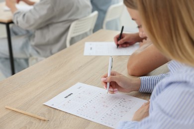 Photo of Students filling out answer sheet at wooden table indoors, closeup. Taking exam
