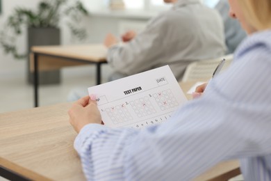 Photo of Students taking exam at wooden table indoors, closeup