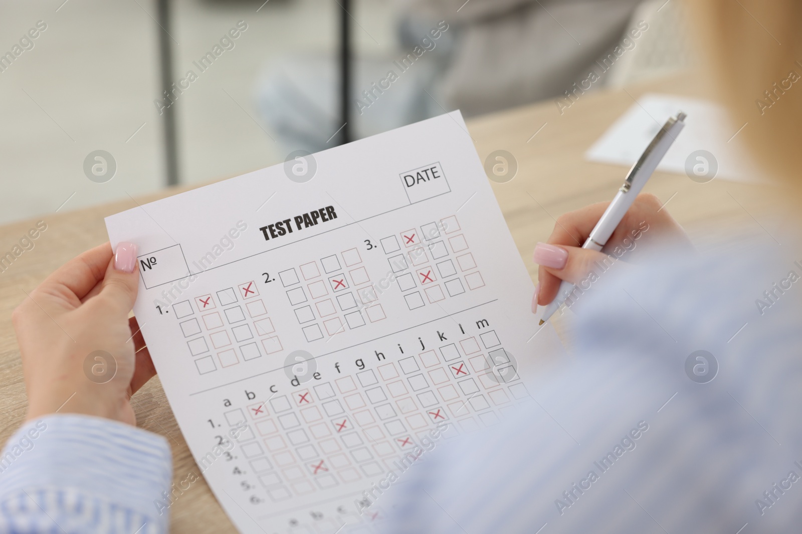 Photo of Student filling out answer sheet at wooden table indoors, closeup. Taking exam