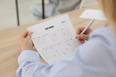 Photo of Student filling out answer sheet at wooden table indoors, closeup. Taking exam