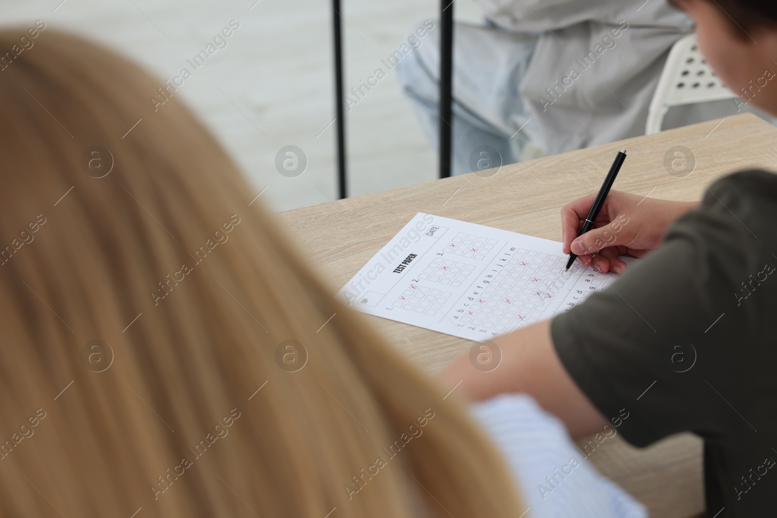 Photo of Students filling out answer sheet at wooden table indoors, closeup. Taking exam