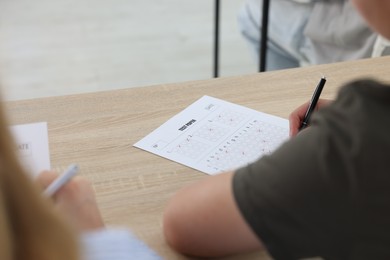 Photo of Students filling out answer sheet at wooden table indoors, closeup. Taking exam