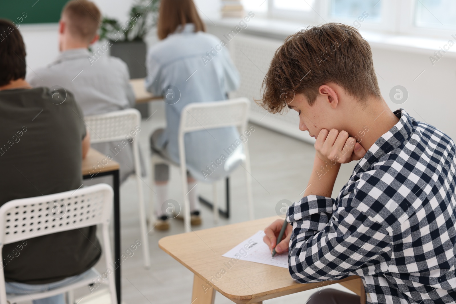 Photo of Students taking exam at wooden table indoors, selective focus