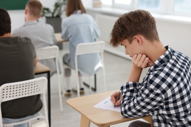 Photo of Students taking exam at wooden table indoors, selective focus