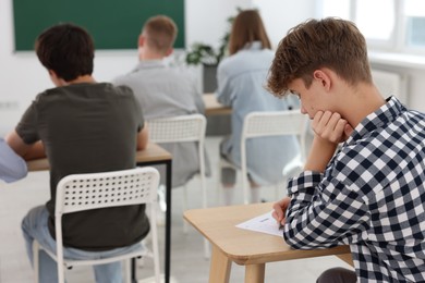 Photo of Students taking exam at wooden table indoors, selective focus