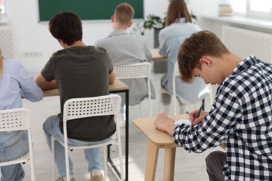 Photo of Students taking exam at wooden table indoors, selective focus
