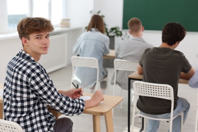 Photo of Students taking exam at wooden table indoors, selective focus