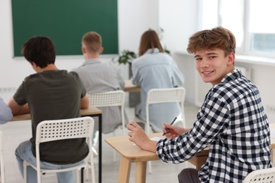 Photo of Students taking exam at wooden table indoors, selective focus