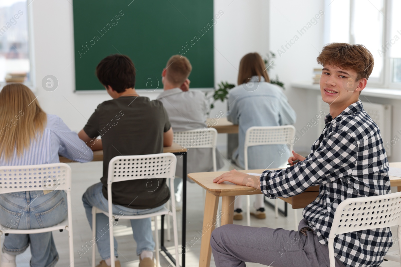 Photo of Students taking exam at wooden table indoors, selective focus