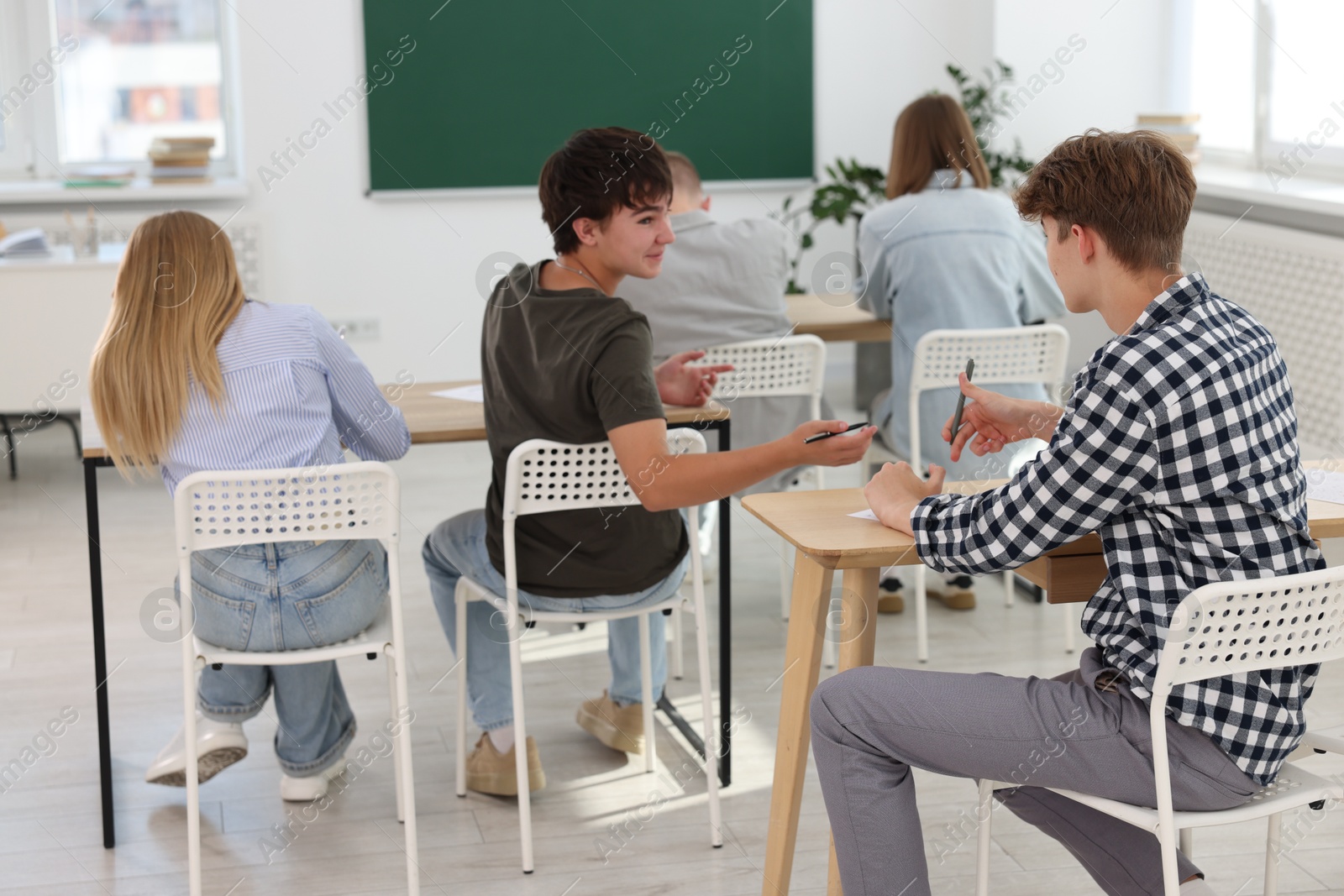 Photo of Students taking exam at wooden table indoors